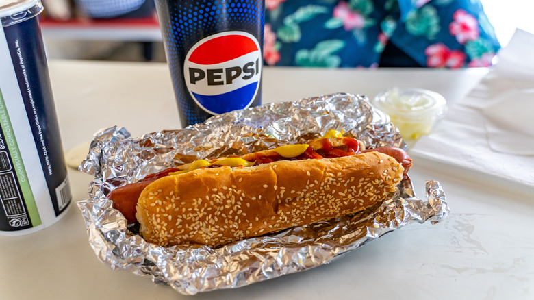 A Costco hot dog sit next to a Pepsi cup