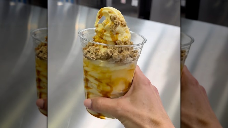A hand holding a sundae made with vanilla soft serve, salted caramel, and cubed churro bites