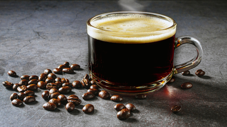 steaming cup of coffee in glass mug with scattered coffee beans