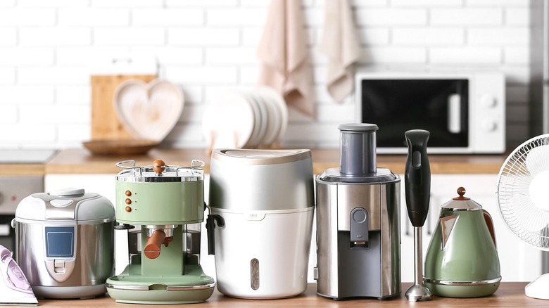 group of kitchen gadgets on a worktop including coffee machine, blender, kettle, deep fryer, small fan and microwave in the background
