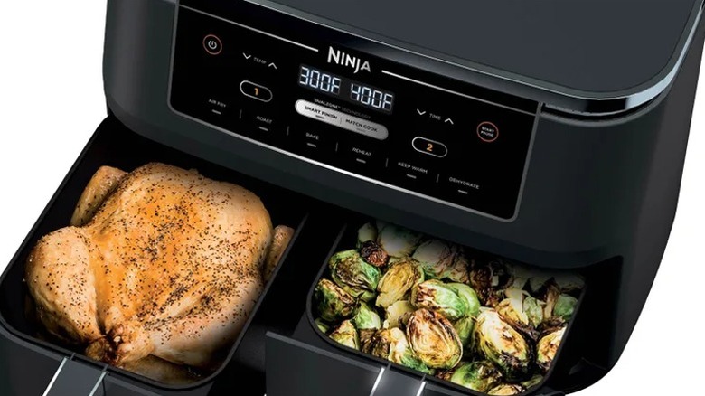 a Ninja air fryer with a whole chicken in one compartment and vegetables in the other