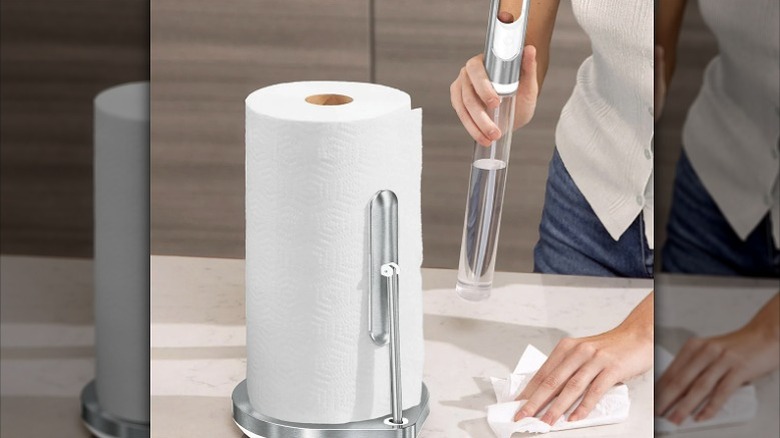 a roll of kitchen towels and a woman holding a disinfectant spray and wiping down the kitchen top