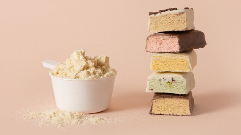 A stack of assorted protein bars next to a scoop of protein powder