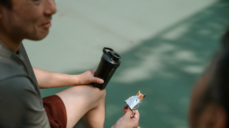 A man holding a water bottle and a protein bar