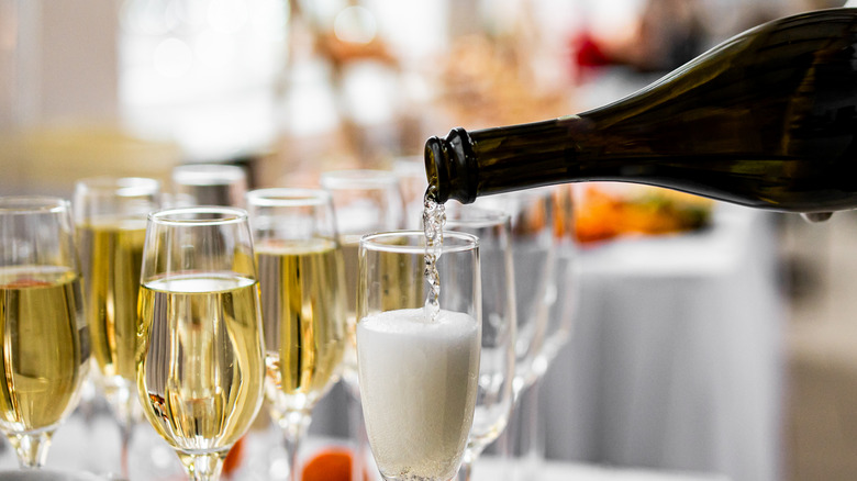 Pouring prosecco into a champagne flute, with filled glasses behind it