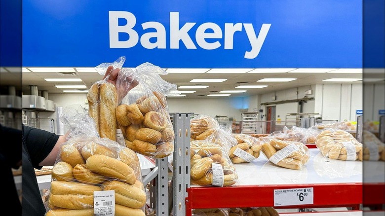 A person holding up a bag of bread in front of a Sam's Club Bakery sign