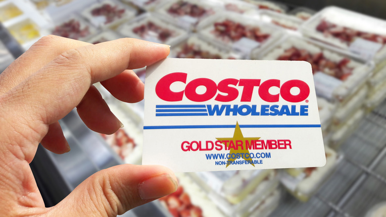 Person holding a Costco membership card in front of a display of desserts