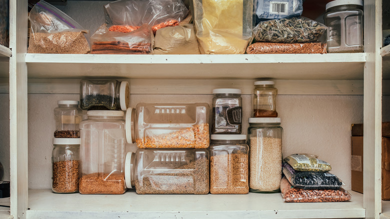 Various pantry staples in clear containers stacked inside of a pantry