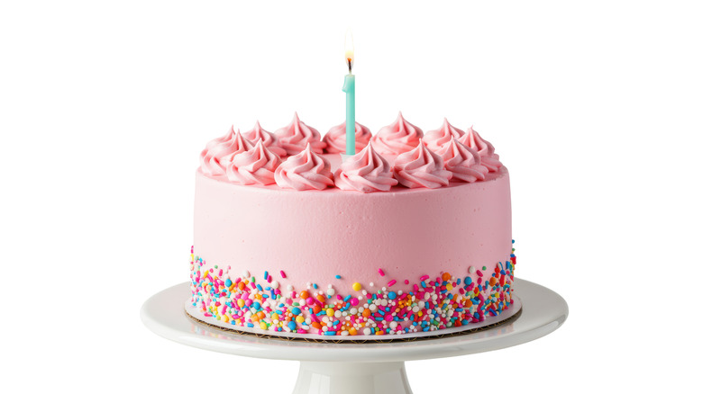 Pink celebration cake on cake stand with blue candle