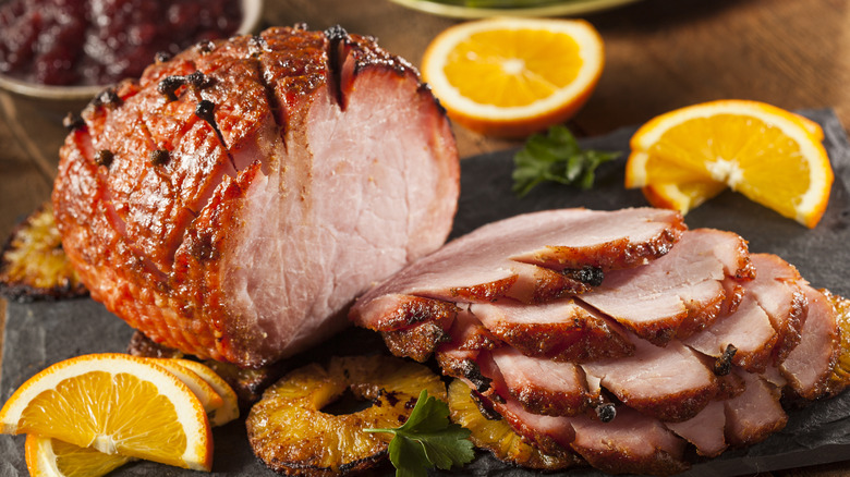 A sliced, honey glazed ham with orange and grilled pineapple garnishes