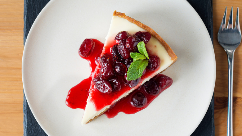 overhead of cheesecake slice on a plate with cherries and sauce