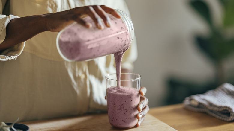 A woman pours a pink smoothie into a glass
