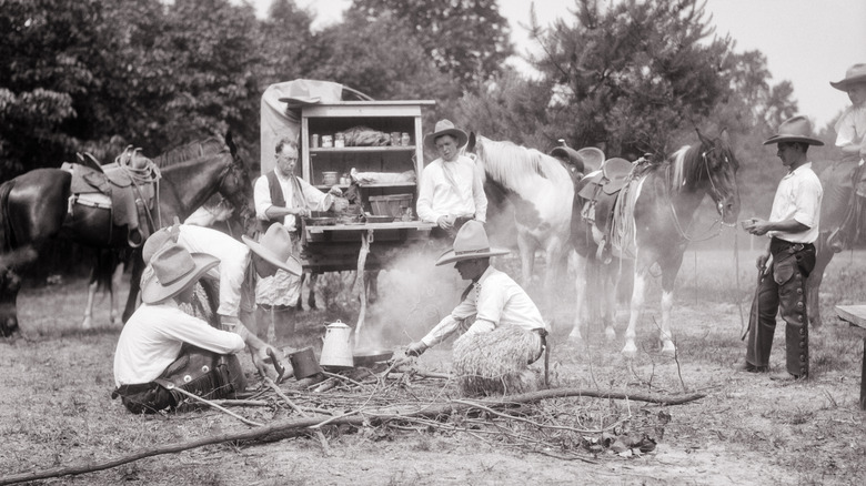 Black and white photo of cowboys around campfire with horses