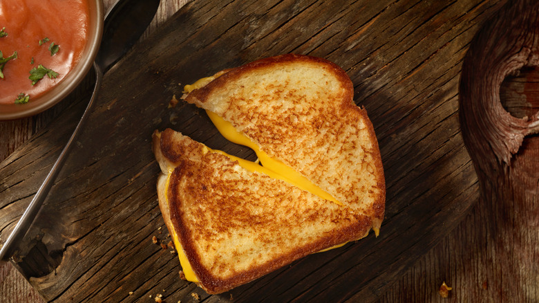 grilled cheese sandwich on dark cutting board next to spoon 