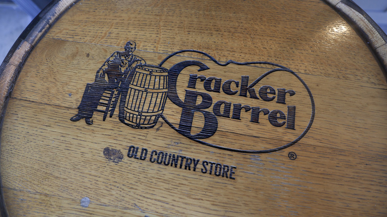 The iconic Cracker Barrel logo carved into the top of a brown barrel