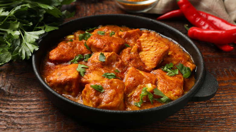A black bowl full of chicken curry on a wooden table