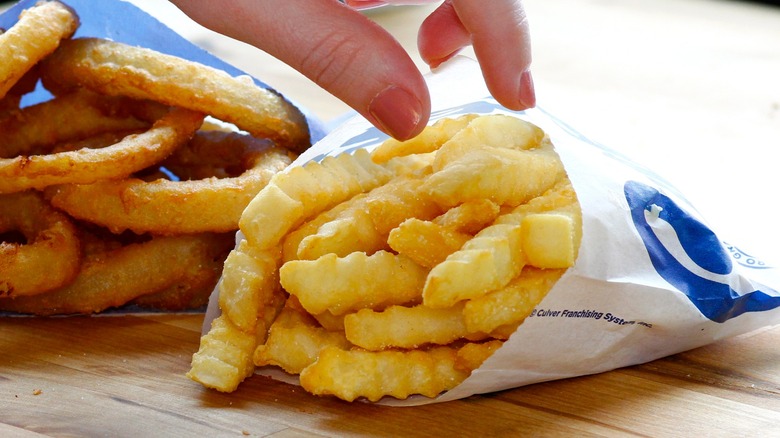 Fingers reaching for Culver's French fries in branded sleeve