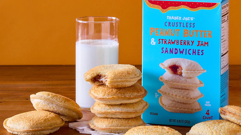 an array of Trader Joe's crustless peanut butter and jam sandwiches on a plate, with a box in the background and a glass of milk on the table