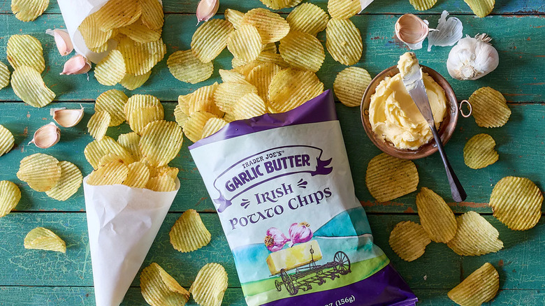 a bag of garlic butter potato chips on a table with scattered chips, bulbs of garlic, and a dish of butter