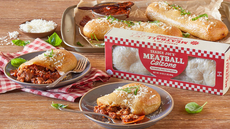 a table setting with two uncut meatball calzones, a box of meatball calzones, and a meatball calzone cut in half and set on two plates