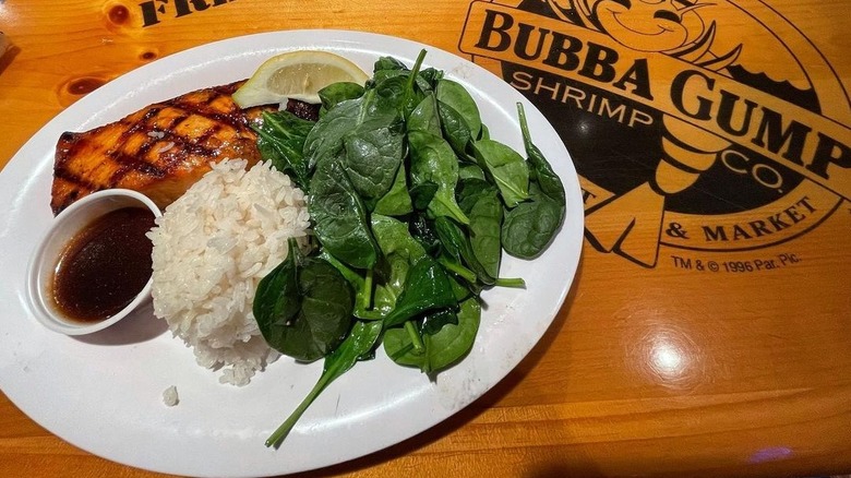 an overhead view of a Maker's Mark glazes salmon with sides of white rice and spinach and an extra ramekin of sauce on a Bubba Gump Shrimp-branded table