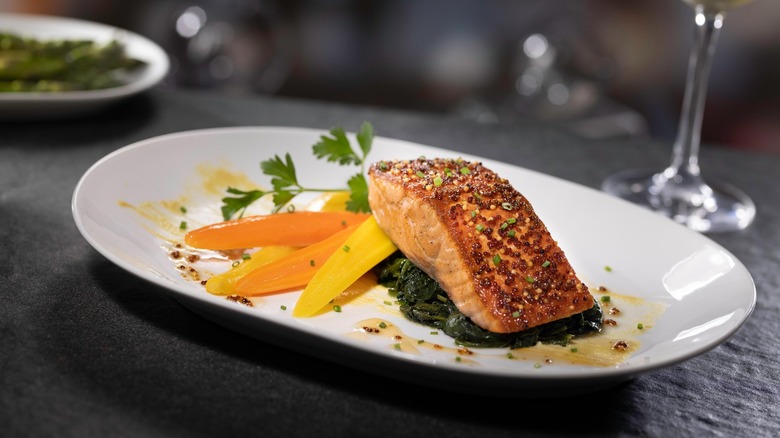 a plate of grilled salmon over sauteed greens and cooked carrots