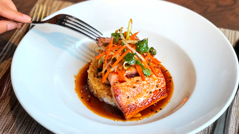 overhead view of a teriyaki salmon from Ocean Prime, topping with pickled vegetables and sitting on rice and sauce, with a fork ready to cut in