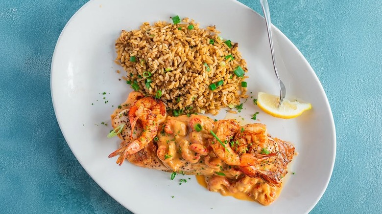 overhead view of a plate of salmon Alexander, topping with shrimp and a cream sauce, and rice with green onions on the side