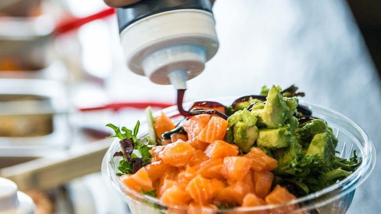 a salmon bowl from Poké Bros, complete with greens and avocado, with sauce being drizzled over the top
