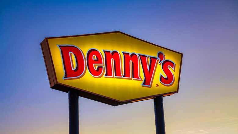 A Denny's sign is illuminated against a blue sky