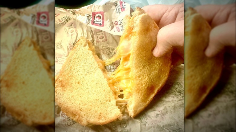 A hand pulling apart a melty grilled cheese on QuikTrip paper