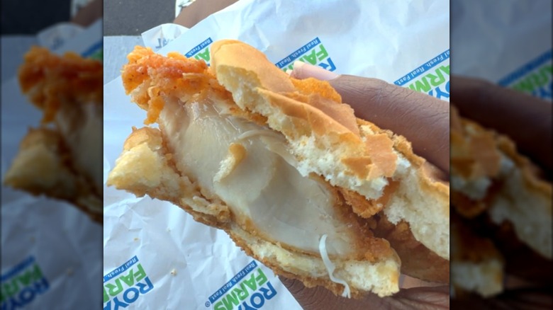 A hand holding a partially eaten piece of fried chicken sandwiched between two waffles