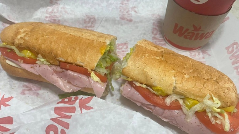 A hoagie with peppered deli meal and veggies on a club roll on Wawa-branded paper