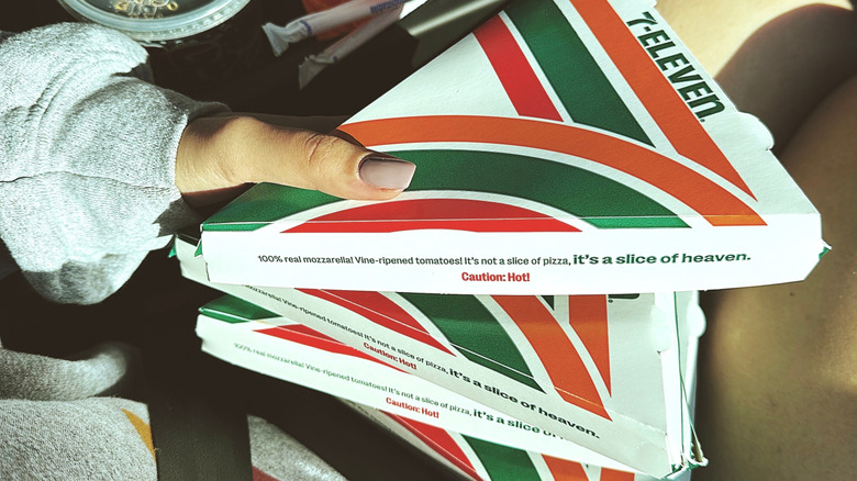 A person holding three 7-Eleven pizza boxes inside a car