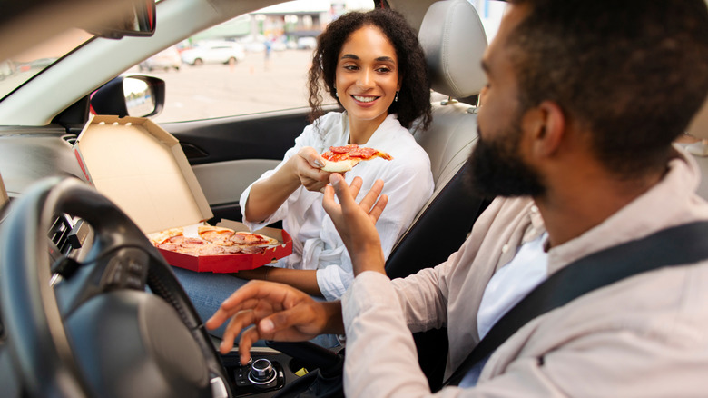 Two people eating pizza from a box within a car