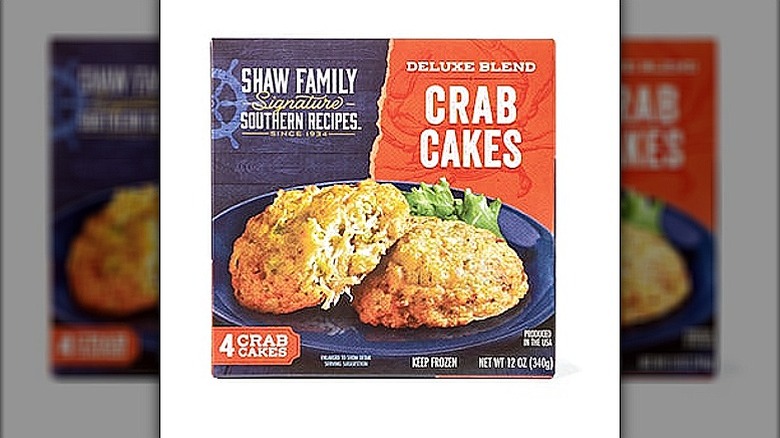 An orange and blue box of Shaw Family Deluxe Blend Crab Cakes, showing 2 crab cakes and garnish on a blue plate