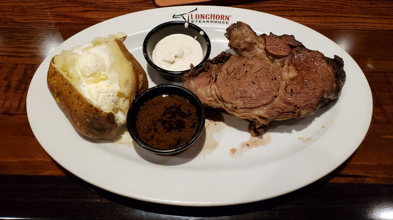 A plate of prime rib with a baked potato on a white plate with the Longhorn Steakhouse logo on it