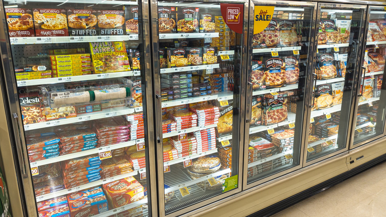 A grocery store freezer section full of various frozen pizzas in boxes