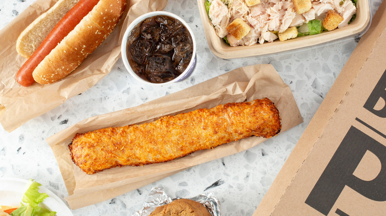 Costco chicken bake, hotdog, soda and Caesar salad sitting on beige wrapping
