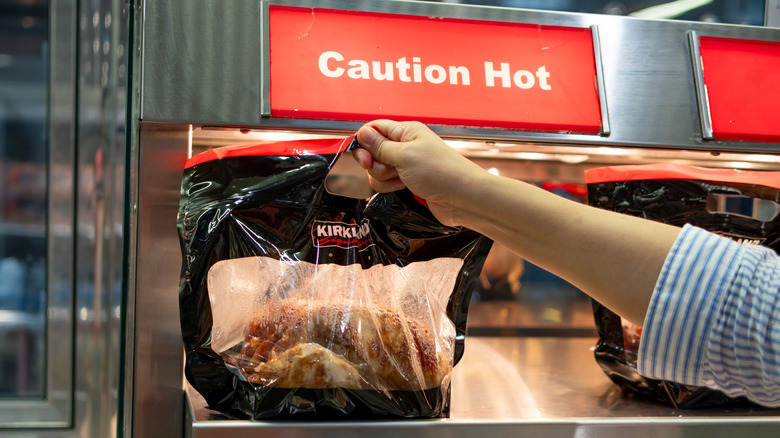 Hand grabbing Kirkland rotisserie chicken from hot bar