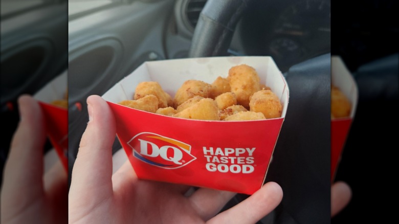 A hand holidng fried cheese curds from Dairy Queen in a red paper box inside a car