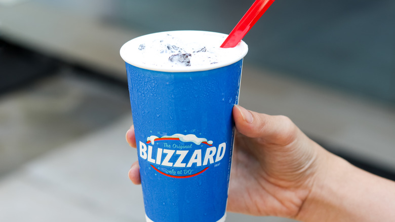 A hand holding a blue Dairy Queen Blizzard cup with a red spoon in it