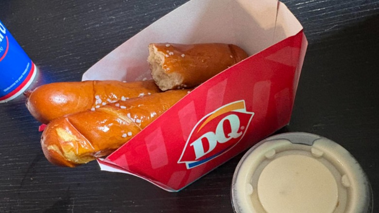 Two full and one half eaten Dairy Queen pretzel sticks in a red paper container with a side of dip