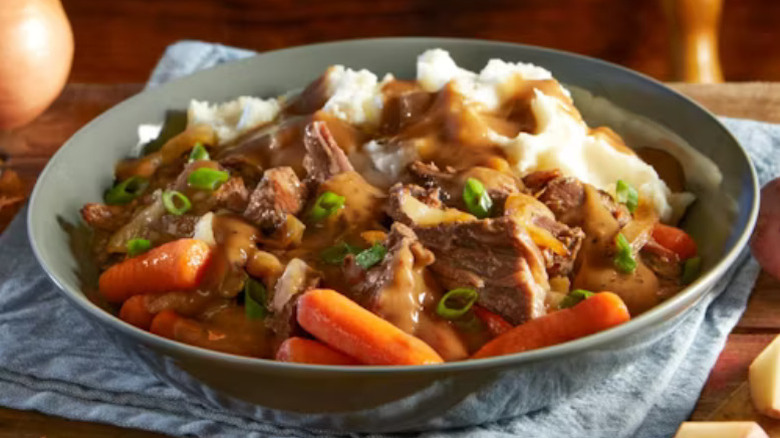 a bowl of pot roast with gravy, carrots, green onion, and mashed potatoes