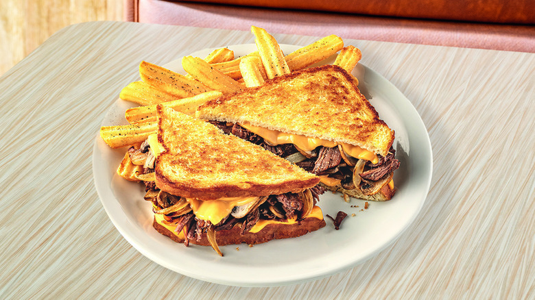 a grilled pot roast sandwich cut diagonally on a plate with crinkle cut fries