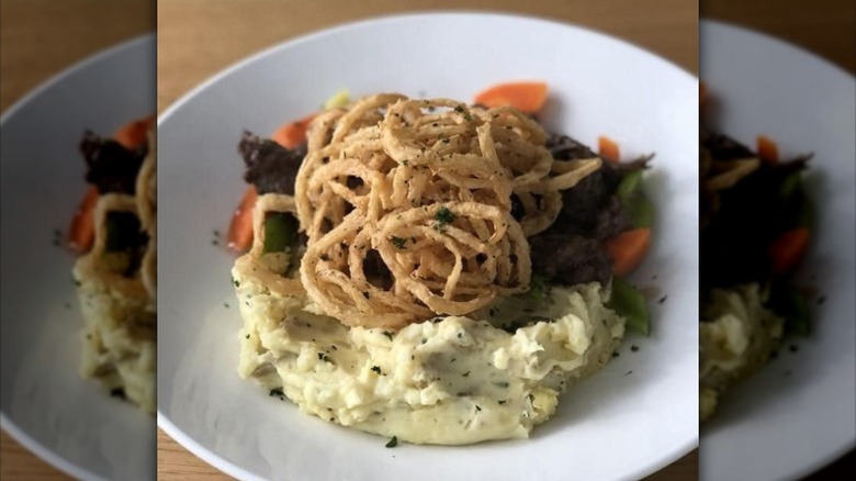 pot roast with carrots on top of mashed potatoes and garnished with fried onion strings