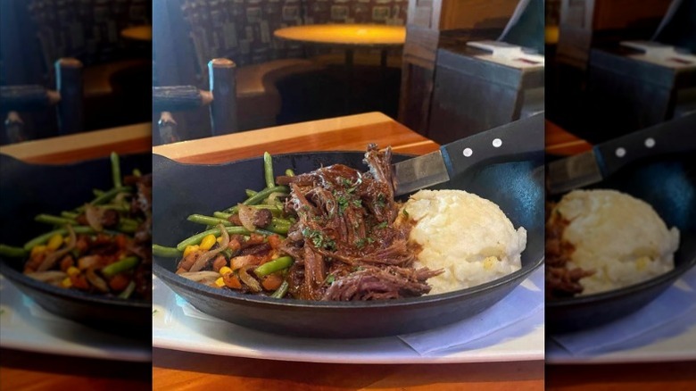 a bowl of pot roast with green beans, corn, carrots, and mashed potatoes on a plate.