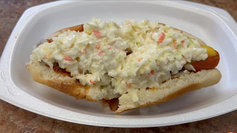 a hot dog with mustard, chili, and cole slaw on a white plate