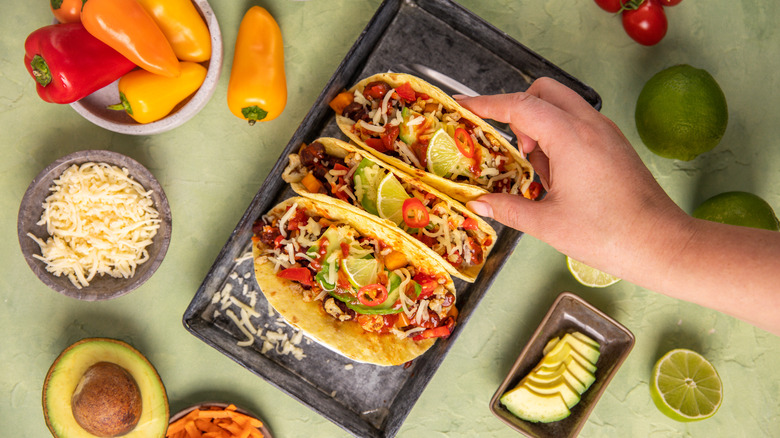 A hand reaches for a taco, in an overhead view of a selection of Mexican foods