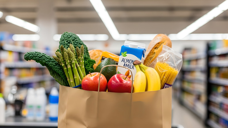 Close-up of a paper grocery bag filled with fresh provisions in front of blurred grocery aisle
